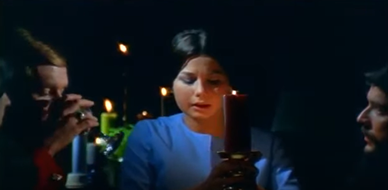 Three people at a table surrounded by candles in the darkness