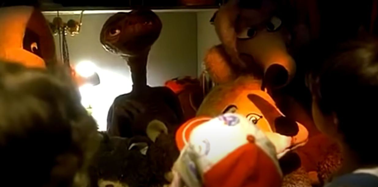 An alien surrounded by stuffed toys