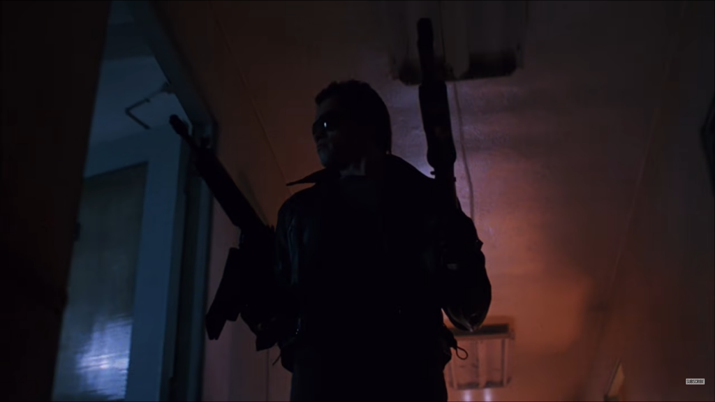 man holding two guns walks down a dark corridor