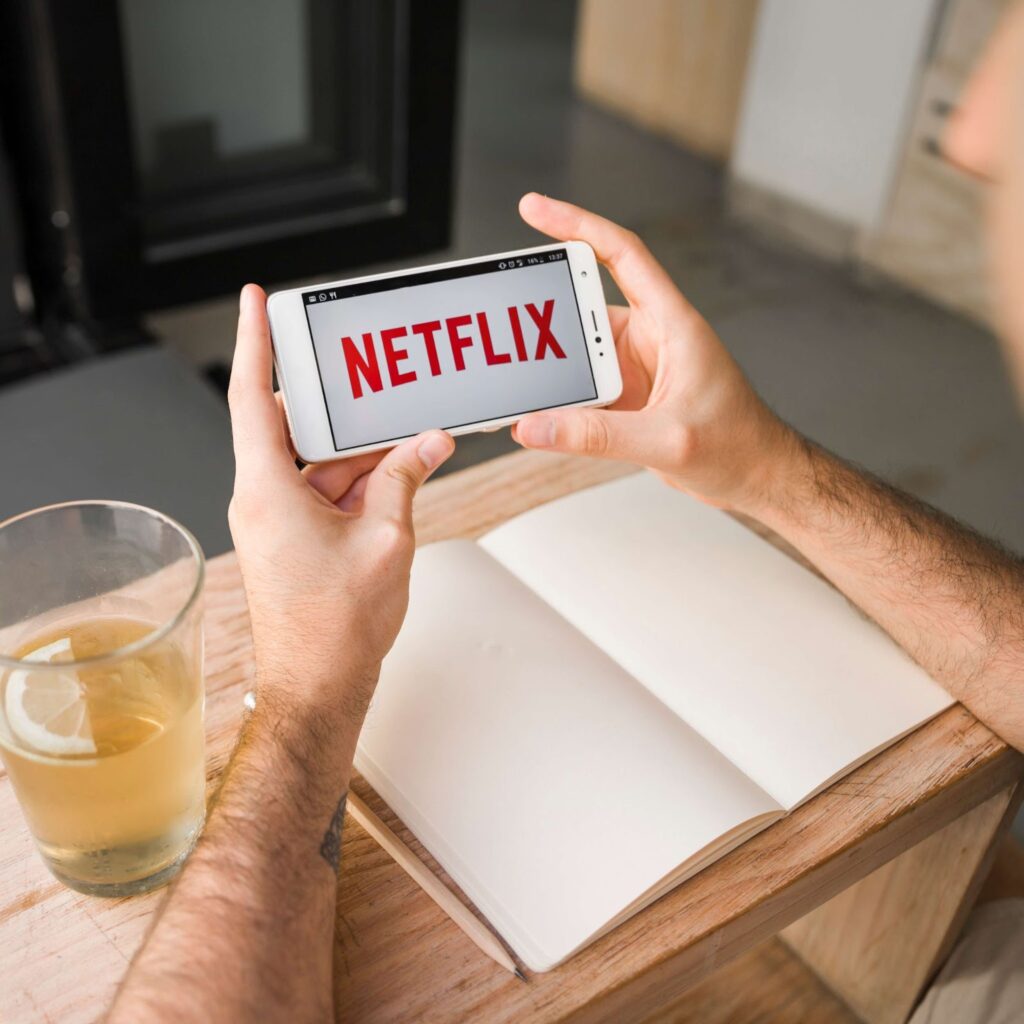 A man is holding a phone with the netflix app open